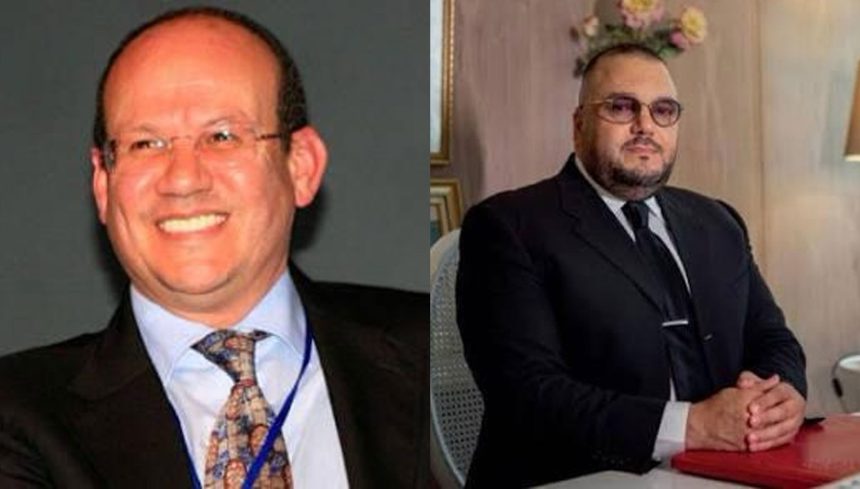 Two men in business suits: left a smiling man with glasses and a blue lanyard; right a seated man in a dark suit at a desk.